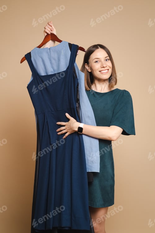 Preview: Young woman holding dresses on hanger, trying to decide what to wear.