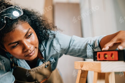 Preview: African American carpenter woman uses a level on a wooden stool in the workshop. Master joiner