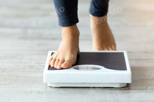 Preview: Unrecognizable young Indian woman stepping on scales to measure her weight at home, closeup of feet