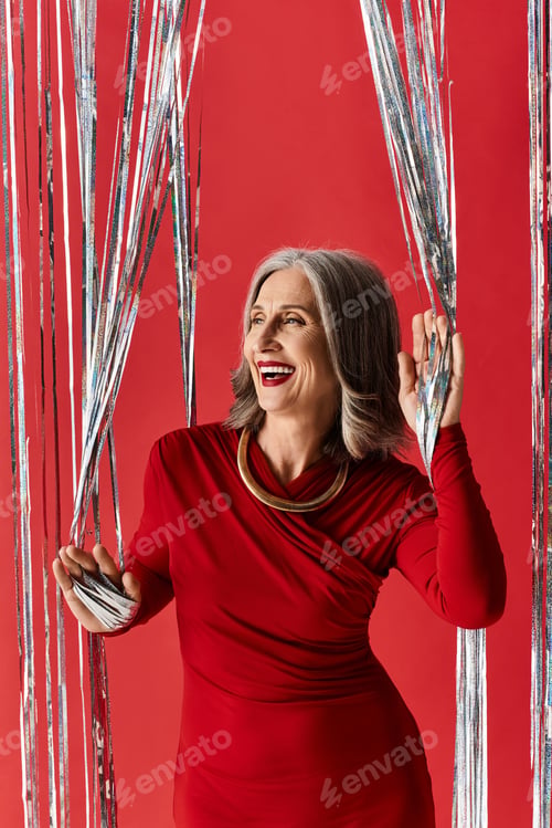 Preview: A joyful mature woman with grey hair celebrating Christmas joyfully in a festive red dress