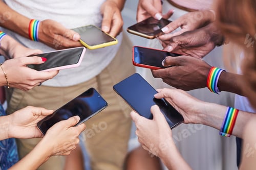 Preview: Group of multiracial people with LGBT rainbow flag wristbands using their mobile phones.