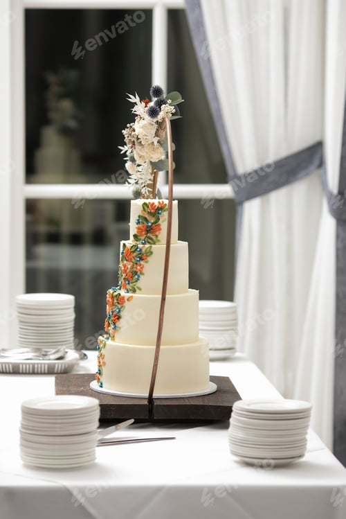 Preview: Four tiered ivory colored wedding cake on table at wedding reception.