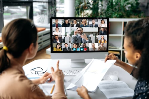 Preview: Virtual meeting online, video call. View over shoulders of two women to a computer screen with