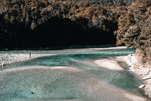 Preview: young caucasian man on the shore of a stony calm shallow river with transparent waters in a very