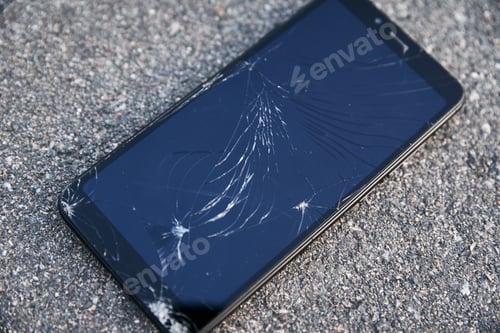 Preview: Damaged smartphone with broken touch screen on asphalt