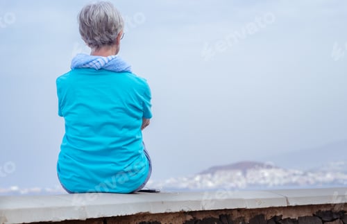 Preview: Rear view of a senior woman sitting face the sea looking at the horizon over water