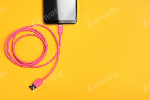 Preview: USB charge cable connected to smartphone on orange background, top view. Space for text