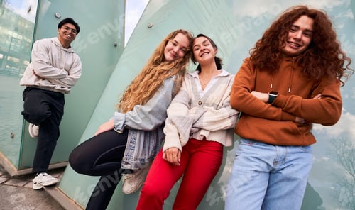 Preview: Group of four diverse teenager students hanging out after school, looking at camera cheerfully.