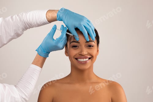 Preview: Young black woman getting beauty cosmetic injection in forehead