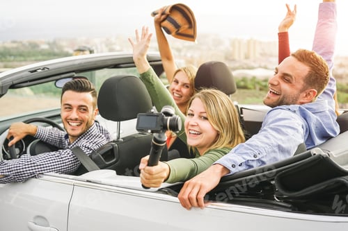 Preview: Happy friends taking photos with selfie stick camera in convertible car in vacation
