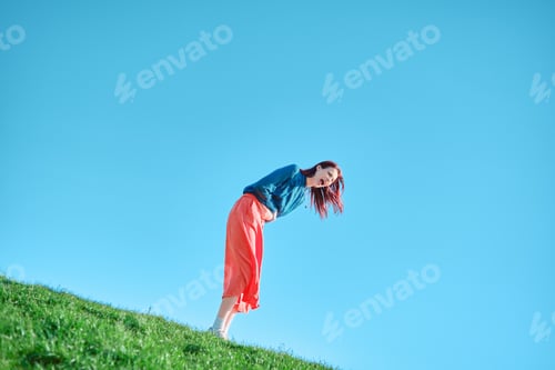 Preview: Teenage girl bent over and screaming on a grassy slope against a clear blue sky.