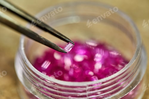 Preview: Ruby held by tweezers on the background of rubies in the bo