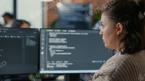 Preview: Over shoulder view of focused database designer writing code looking at multiple computer screens