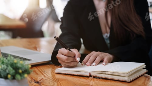 Preview: Close up hand of woman hand holding pen taking note and working with laptop at the table office