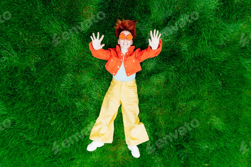Preview: Top view happy smiling redhead Woman with freckles and red orange gerbera Flower glasses on grass.