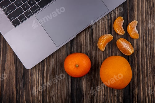 Preview: top view oranges with peeled wedges and a laptop on a wooden background