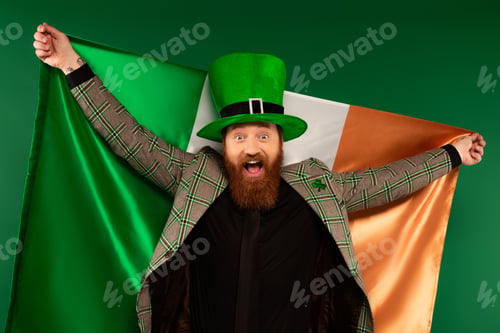 Preview: Excited bearded man in hat holding Irish flag isolated on green