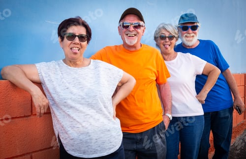 Preview: Happy group of four friends standing against a wall smiling and gesturing with funny faces