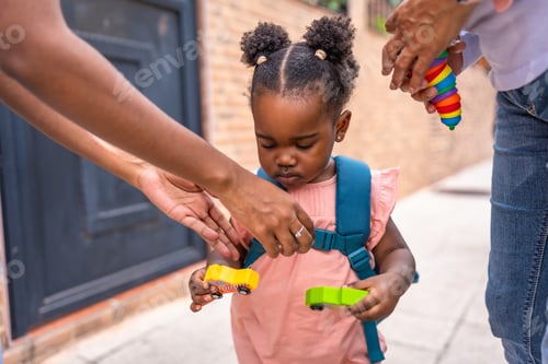 Preview: Baby african girl with schoolbag holding car toys at street