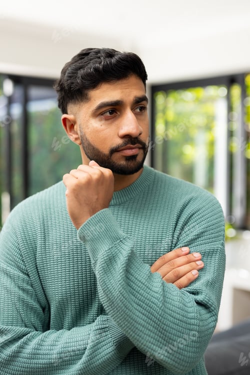 Preview: Thinking deeply, Indian man in green sweater standing with hand on chin