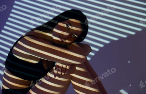 Preview: Sitting on the floor. Beautiful young woman is in projector neon lights in the studio