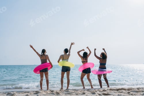 Preview: Teenagers laughing and playing in the sea with colorful swim rings, enjoying youthful summer fun.