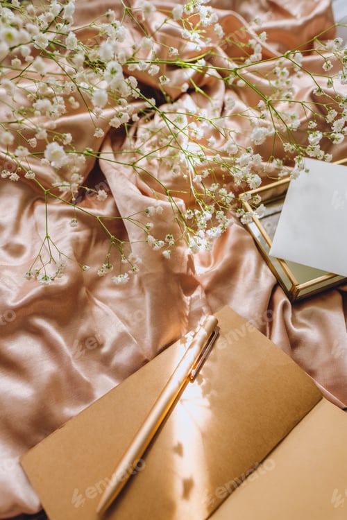 Preview: Spring composition, white gypsophila flowers with notebook and pen on the gold satin fabric