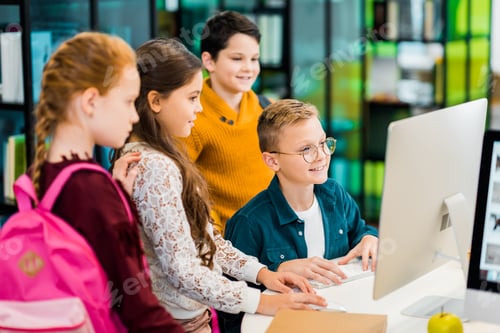 Preview: smiling schoolchildren using desktop computer together in library