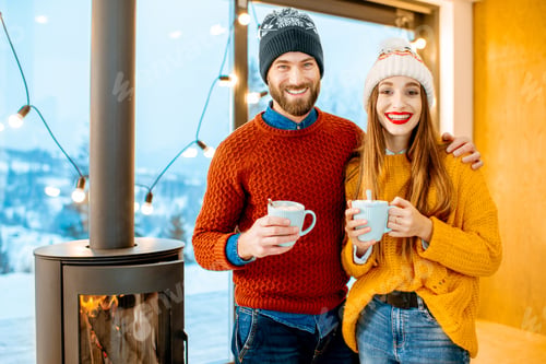 Preview: Couple with hot drinks near the fireplace during winter time