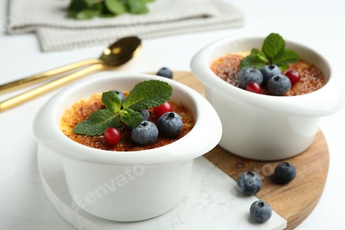 Preview: Delicious creme brulee with berries and mint in bowls on white table, closeup