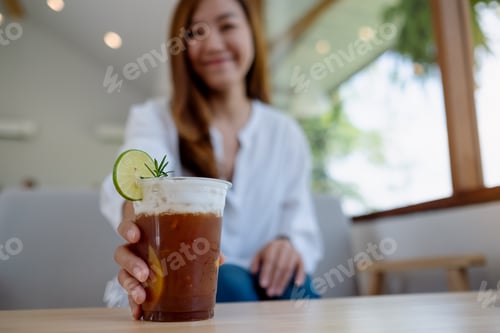Preview: A beautiful young asian woman holding and grabbing a glass of iced coffee on the table