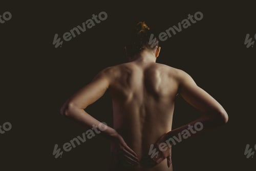Preview: Nude woman with a back injury on black background