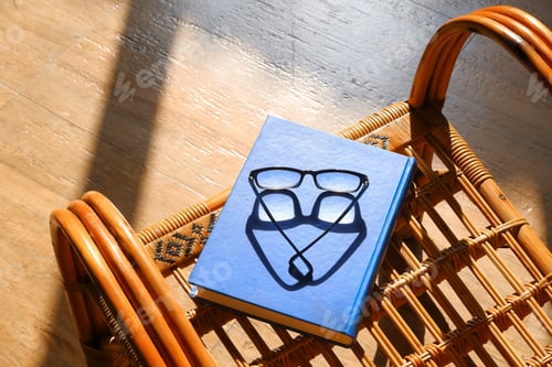 Preview: Textbook with eyeglasses on a vintage rattan chair under natural sunlight in sunlit room