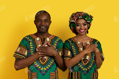 Preview: Cheerful african lovers in traditional costumes holding hands on chest