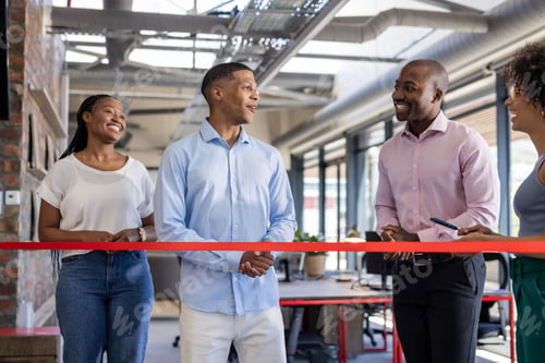 Preview: Colleagues celebrating office opening, smiling and chatting near red ribbon indoors