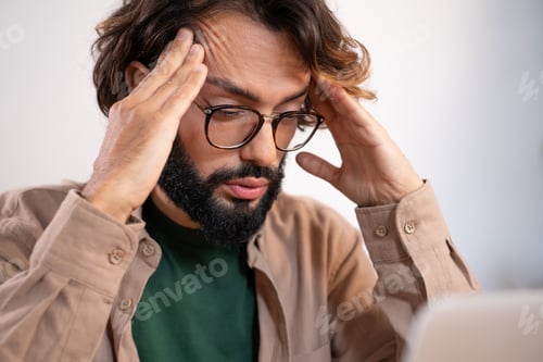 Preview: Worried man suffering from headache at work thinking about problems and project deadline.