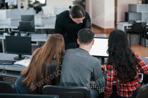 Preview: Together near one monitor. Group of young people in casual clothes working in the modern office
