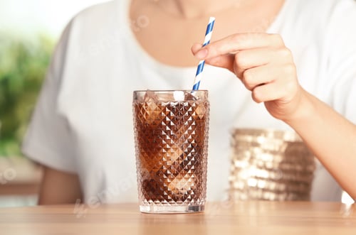 Preview: Woman with glass of tasty refreshing cola at table, closeup view