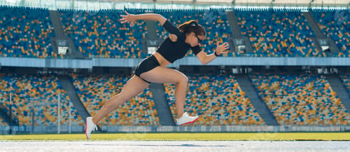 Preview: Side view of a female athlete sprinting on a running track in a track and field stadium.