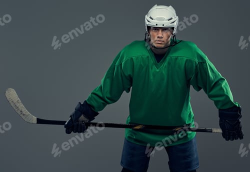 Preview: Hockey player wearing black protective uniform holds a hockey stick on a gray background.