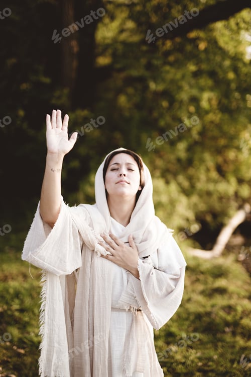 Preview: Vertical shot of female wearing a biblical robe with her hands up towards the sky praying