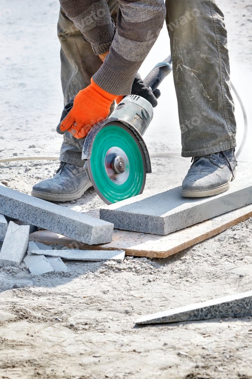 Preview: A builder uses a grinder and diamond cutting disc to cut granite blocks. Vertical image.