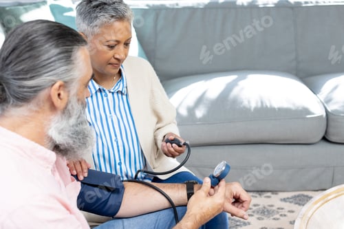 Preview: Checking blood pressure, senior woman assisting man with monitor on couch, copy space