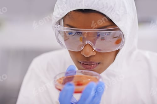 Preview: Careful observation. A young scientist in protective clothing examining a petri dish in her lab.