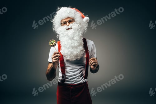 Preview: cheerful santa claus in eyeglasses standing with colorful lollipop isolated on grey background