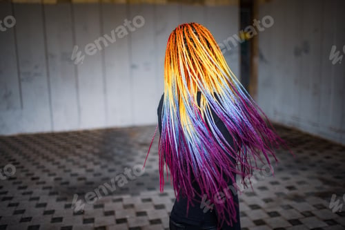 Preview: Unusual elegant girl in a black simple dress with bright makeup and multi-colored braids posing
