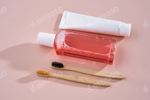 Preview: Pink mouthwash, toothpaste and toothbrushes on a pink background.