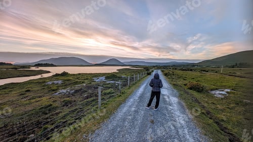 Preview: Girl hiker on Empty rural road by lake and mountains at Connemara national park, Galway, Ireland