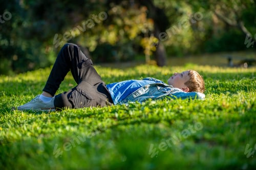Preview: Young cheerful child relaxing in a park. Smiling child laying down on the grass in a garden.