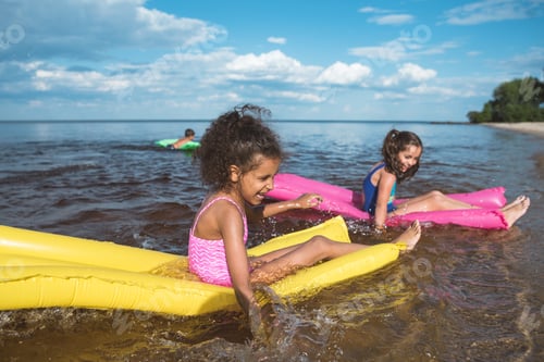 Preview: multicultural happy girls swimming together on inflatable mattresses at sea